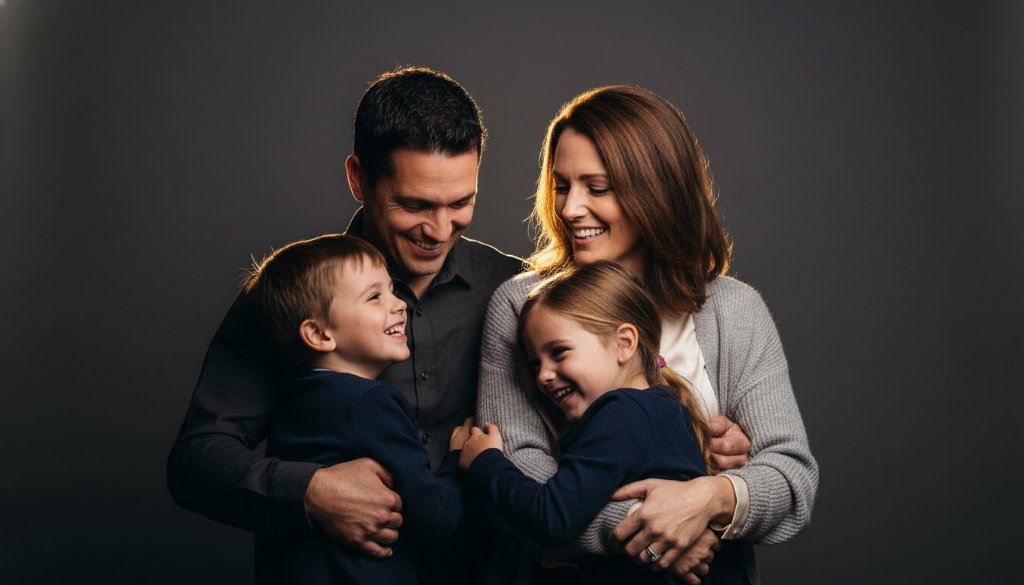 A joyous Boronia family of four, parents embracing two laughing children, captured in a modern studio portrait photography Boronia families style, with dramatic lighting creating a warm, intimate atmosphere, showcasing genuine connection.