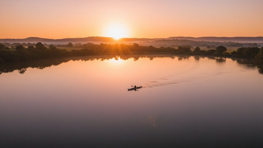 An epic moment captured by Moe Victoria drone photography elevated perspectives, showing the sunrise over Lake Narracan with a lone kayaker, dramatic light, and lush green surrounds.