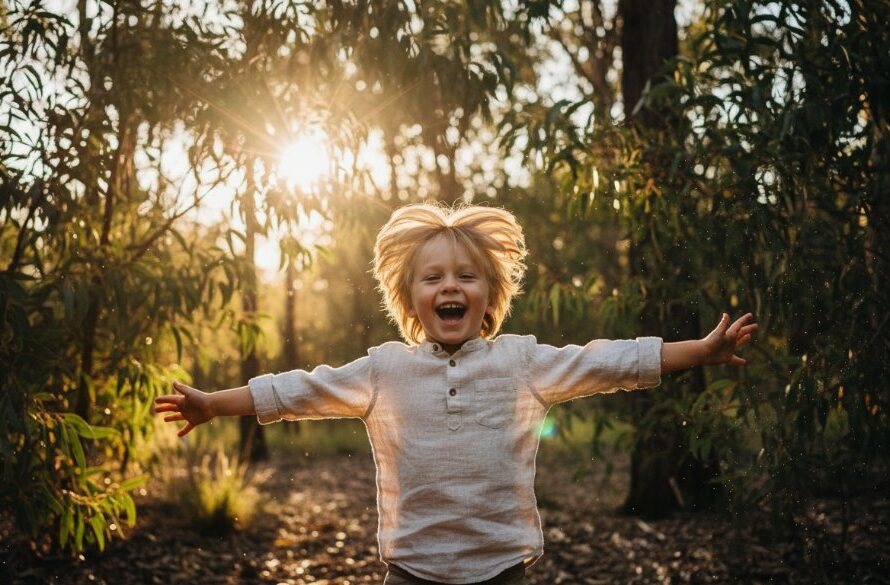 A heartwarming, epic moment captured of a child laughing joyfully amidst the dappled sunlight of Woowookarung Regional Park in Mount Clear, Victoria, showcasing professional Mount Clear kids photography natural light outdoor portraits with dramatic lighting and vibrant colours.