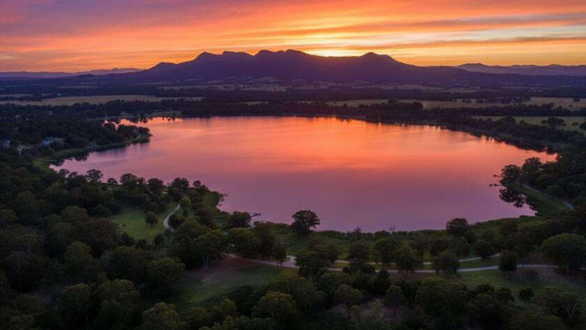 An epic aerial view captured by Narre Warren drone photography for breathtaking landscape visuals, showing the vibrant colours of a sunset over Lysterfield Lake with the distant Dandenong Ranges, expertly lit and colour-graded.