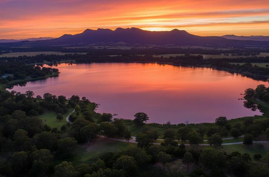 An epic aerial view captured by Narre Warren drone photography for breathtaking landscape visuals, showing the vibrant colours of a sunset over Lysterfield Lake with the distant Dandenong Ranges, expertly lit and colour-graded.