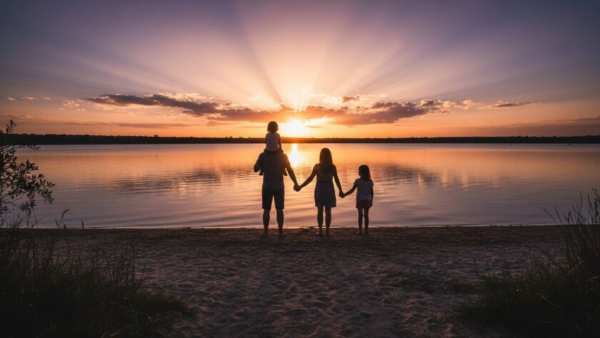 An emotive wide-angle shot by a Newborough family photographer capturing genuine moments, featuring a family silhouetted against a golden hour sunset over the tranquil Lake Narracan, parents embracing children as they laugh, with warm, cinematic lighting and professional colour grading.