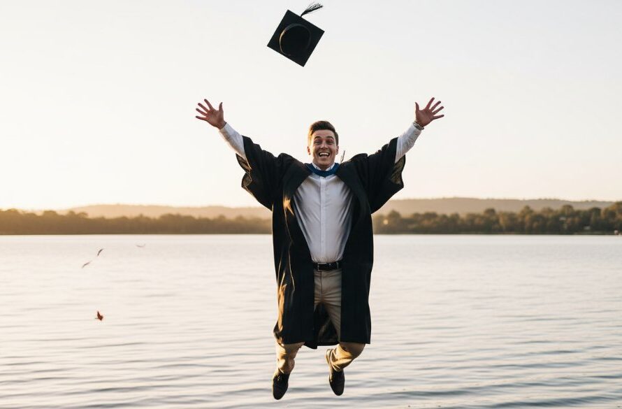A triumphant graduate in academic regalia, captured mid-air in a celebratory jump, silhouetted against a breathtaking golden hour sunset over Lake Narracan, reflecting the joy of their 'Newborough Victoria graduation photography celebrations.' The scene is professionally lit and colour-graded, exuding an epic, cinematic feel.