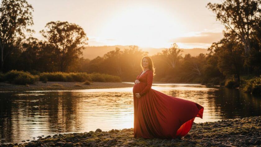 A stunning Orbost riverside maternity photoshoot Victoria featuring a radiant mother-to-be, silhouetted against a golden hour sky by the Snowy River, her flowing dress catching the soft breeze, evoking an epic moment of serene anticipation.