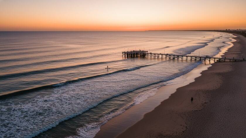 An epic moment of a drone capturing Parkdale coastal drone photography stunning aerial views, featuring golden hour light illuminating the serene beach, distant pier, and sparkling azure waters from a high vantage point.