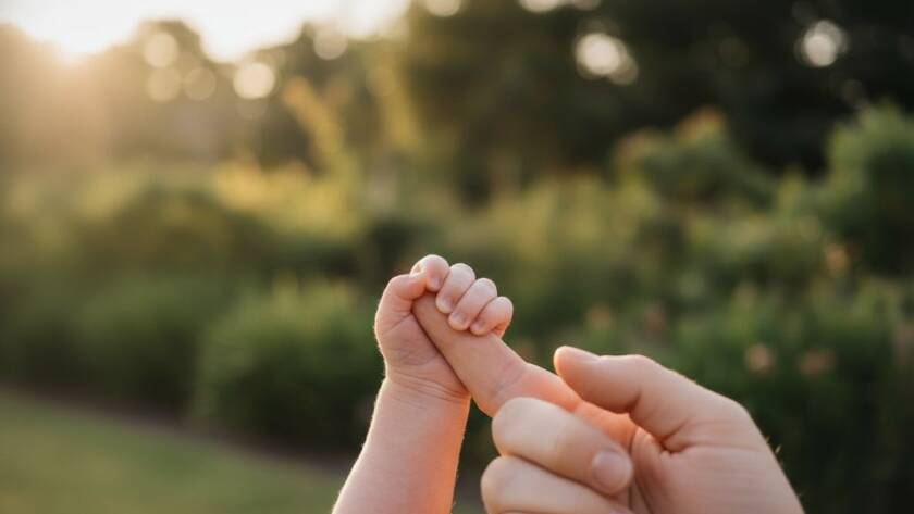 A heartwarming, cinematic close-up of a newborn baby's tiny hand gently grasping a parent's finger, set against a softly blurred, golden-hour backdrop of a serene park in Melton West, evoking the precious newborn photography Melton West families cherish. Dramatic, soft light highlights the delicate details.