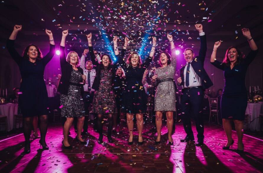 A wide-angle, vibrant shot of guests celebrating under colourful lights at a Dandenong North community hall, perfectly capturing professional Dandenong North party photography unforgettable moments with laughter and movement.