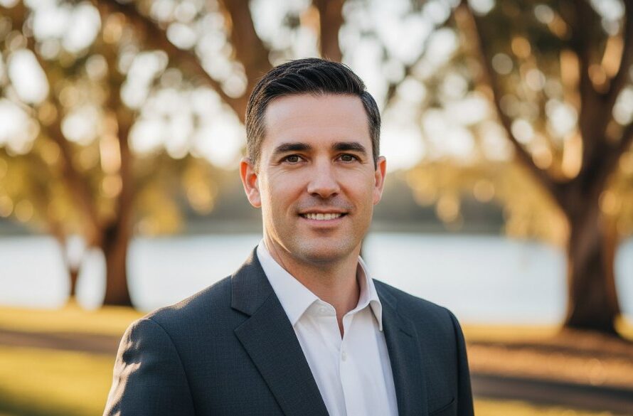 A confident professional headshot in Brown Hill, Victoria, featuring a businessperson against a soft, sun-dappled backdrop near Lake Esmond, embodying career advancement and professionalism, with warm, golden hour lighting and a shallow depth of field.