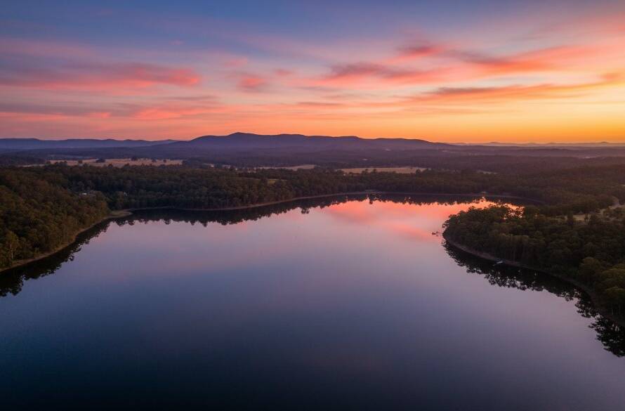 An epic moment captured with Ringwood Victoria aerial photography breathtaking views, showing a vibrant sunset over the Maroondah Reservoir near Ringwood, with golden light illuminating lush trees and a tranquil water surface, shot from a drone perspective with cinematic colour grading.