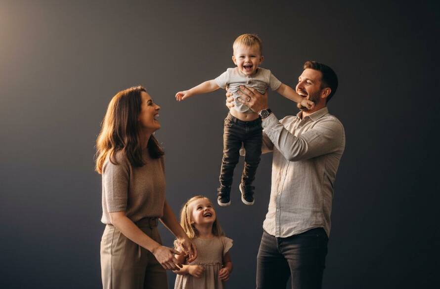 An emotionally resonant, epic moment photograph capturing a family laughing joyfully during a Ringwood Victoria bespoke family studio photography session, with dramatic backlighting and a warm, inviting atmosphere.