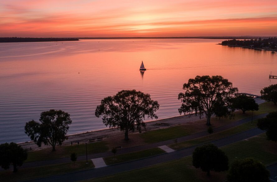 An epic moment captured with Rippleside drone photography for stunning waterfront views, showcasing a vibrant sunset over Corio Bay with the Rippleside foreshore and a lone kayaker in the foreground, professional colour grading and cinematic appeal.