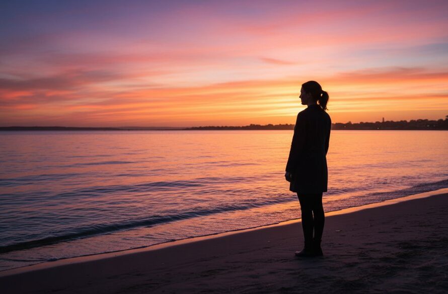 An aerial perspective showcasing Rippleside fine art photography capturing coastal serenity, featuring a lone figure contemplating the dramatic sunrise over Corio Bay, with soft, golden light illuminating the gentle waves and the distant silhouette of the city, professionally colour-graded for a cinematic feel.