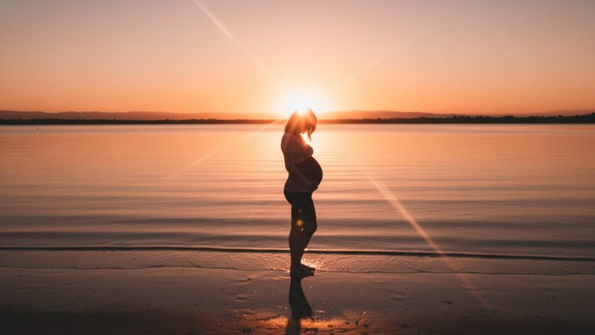 A pregnant woman, beautifully silhouetted against a dramatic Rippleside maternity photography sunset, cradles her belly on the shore of Corio Bay, capturing an epic moment of serene anticipation and golden light.