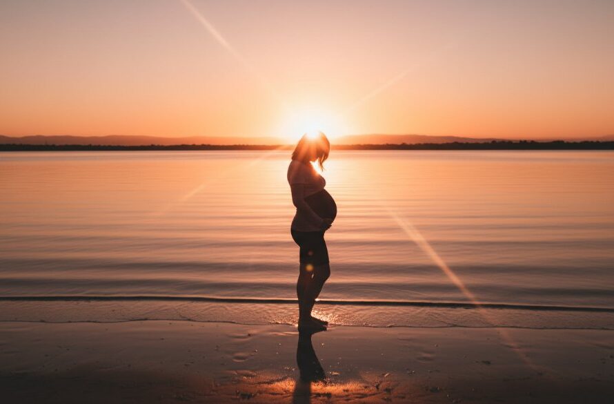 A pregnant woman, beautifully silhouetted against a dramatic Rippleside maternity photography sunset, cradles her belly on the shore of Corio Bay, capturing an epic moment of serene anticipation and golden light.