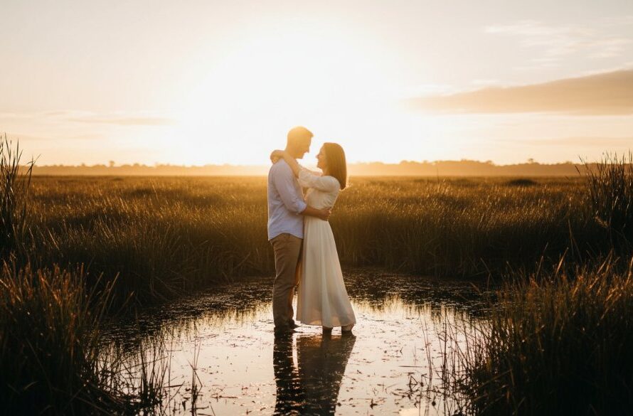 A couple embracing passionately at sunset during their Sale Victoria wetlands engagement photoshoot, with dramatic golden hour light filtering through tall reeds and reflecting on calm water, capturing an epic moment of love and serenity.