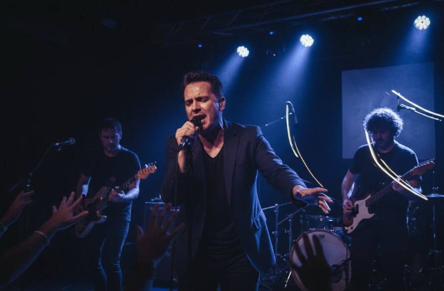 A dynamic wide-angle shot capturing the electric energy of a guitarist mid-solo on stage at a cosy Seddon venue, bathed in dramatic magenta and blue stage lights, illustrating Seddon live music photography tips for emerging artists.