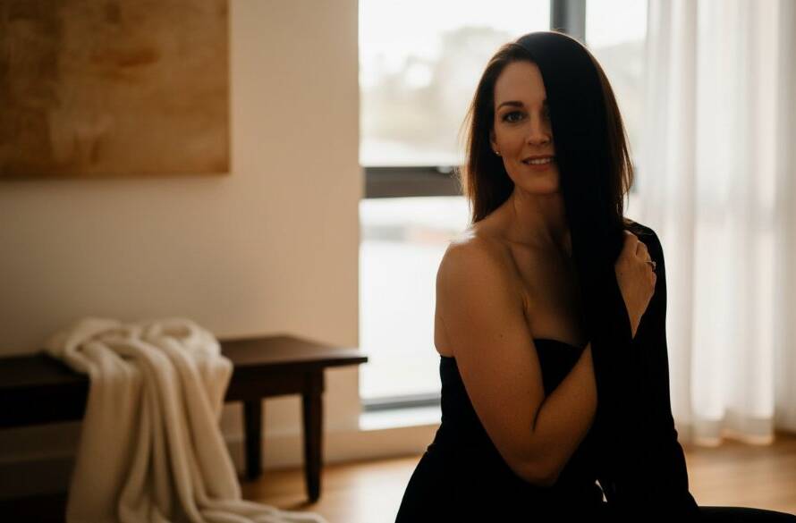 An empowering and sensual Rowville boudoir photography experience captured, featuring a woman elegantly posed in a luxurious, softly lit studio, with dramatic shadows highlighting her silhouette, evoking confidence and grace.