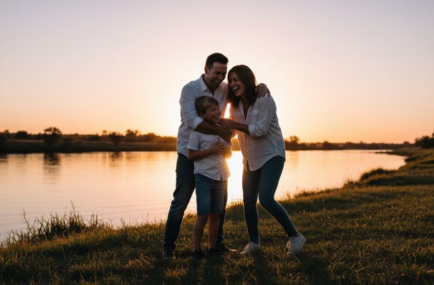 A joyous family laughing genuinely during a Seymour candid photography session, silhouetted by the warm glow of a sunset over the Goulburn River, capturing an epic unposed moment of connection.