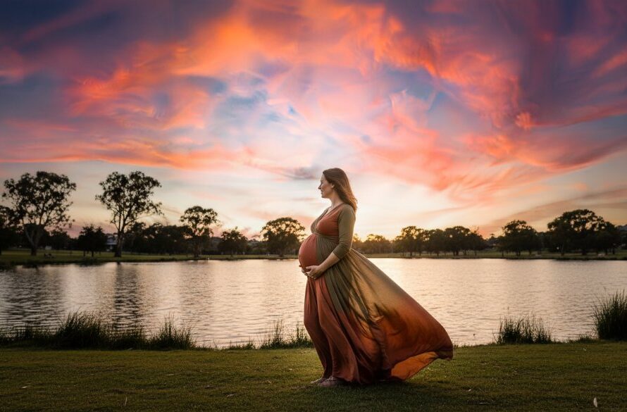 A pregnant woman, in a flowing amber gown, stands silhouetted against a golden Shepparton sunset, her hands cradling her baby bump, embodying the serene and epic Shepparton Victoria scenic maternity photoshoot experience.