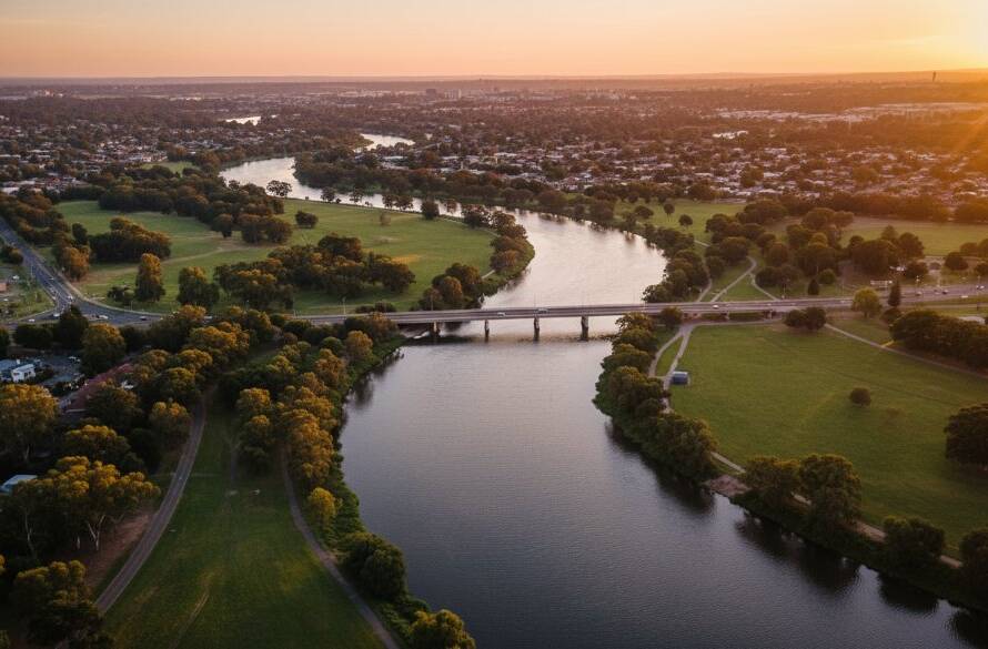 St Albans Drone Photography Victoria Landscapes capturing an epic, golden hour aerial view of the Sunshine Avenue bridge arching over the Maribyrnong River with distant St Albans rooftops bathed in warm light, showcasing the serene urban-natural blend.