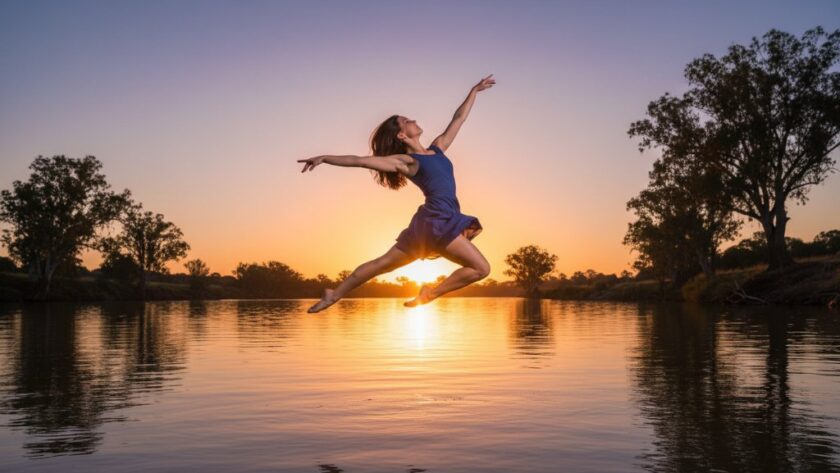 A dynamic and elegant Swan Hill dance photography capturing graceful movement of a professional contemporary dancer mid-air, silhouetted against a golden hour sunset over the Murray River, showcasing power and elegance with professional lighting.