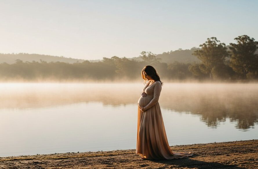 A glowing pregnant woman, gracefully posed amidst the soft, ethereal mist of a sunrise over Lake Daylesford, capturing a timeless Hepburn Springs maternity photoshoot experience with dramatic cinematic lighting.