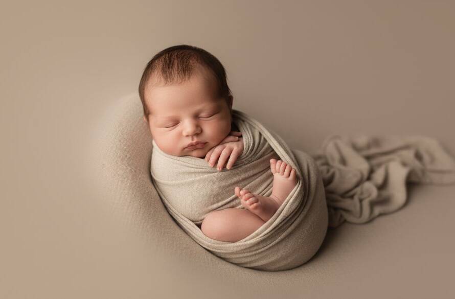 An emotionally resonant and visually stunning epic moment photograph of a newborn baby peacefully sleeping, swaddled in soft, natural fibres, held gently in a parent's hands, bathed in dramatic, soft golden hour light filtering through a window in a Bentleigh home. The focus is on the baby's delicate features, with a shallow depth of field, showcasing timeless newborn photography Bentleigh artistry and professional colour grading.