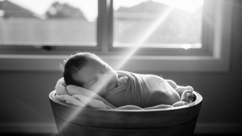 A close-up, dramatic, black and white photograph of a newborn baby's tiny hand gently grasping a parent's finger, bathed in soft, ethereal light filtering through a window in a warm Noble Park home, embodying the tender connection and timeless newborn portraits Noble Park families adore.