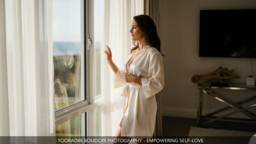 A stunning, professionally lit and colour-graded photograph featuring a woman embracing her unique beauty, bathed in soft, natural light filtering through sheer curtains in a luxurious, private Tooradin setting, capturing an intimate boudoir photography for empowering self-love moment of quiet confidence and elegance.