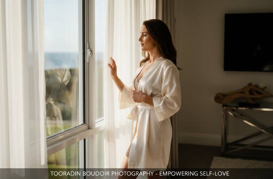 A stunning, professionally lit and colour-graded photograph featuring a woman embracing her unique beauty, bathed in soft, natural light filtering through sheer curtains in a luxurious, private Tooradin setting, capturing an intimate boudoir photography for empowering self-love moment of quiet confidence and elegance.