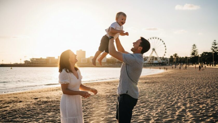 A heartwarming, candid photograph capturing a family's joyous laughter on Eastern Beach, Geelong, with the golden hour sun creating a dramatic flare, embodying unposed moments Geelong candid family photography at its best. The parents are playfully swinging their child, faces full of genuine happiness against the stunning coastal backdrop.
