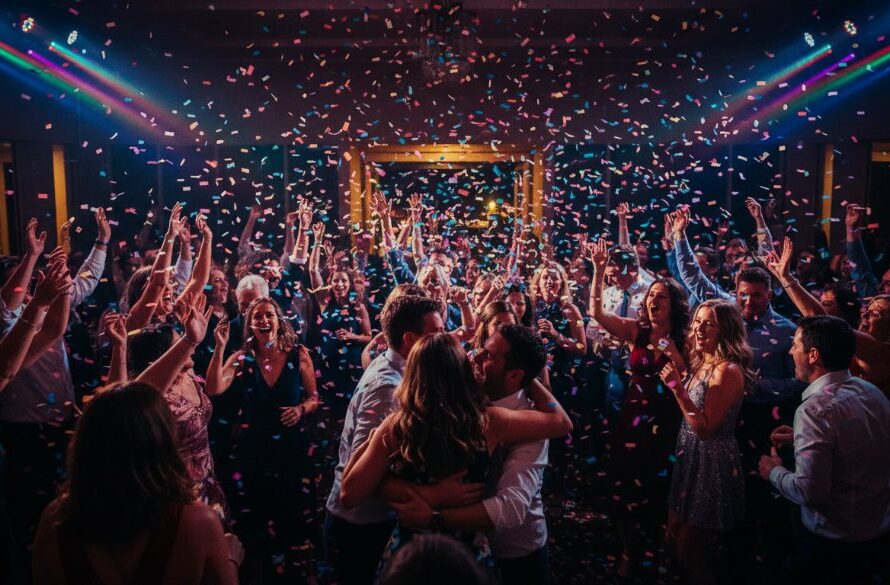 Dynamic wide shot capturing the vibrant party photography Traralgon Victoria special events atmosphere: a group of guests on a dance floor, mid-laughter and movement, confetti falling, illuminated by colourful disco lights at a Traralgon venue, embodying pure joy and celebration.