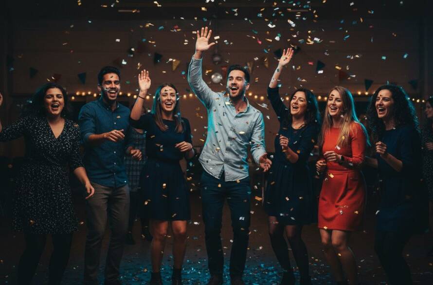 A candid, vibrant St Albans party photography Victoria shot capturing a group of friends laughing and dancing under colourful lights at a community hall, confetti frozen in mid-air, creating an epic moment of pure joy and celebration.