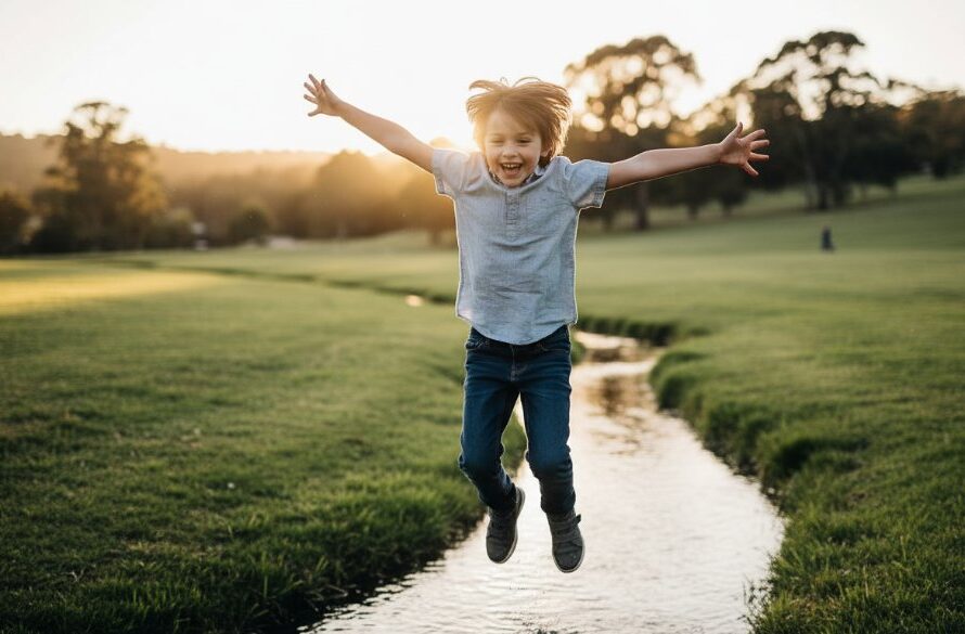 An 'epic moment' photograph of a child mid-air, laughing joyfully as they jump over a small stream in a sun-dappled Wallan park, embodying the spirit of Wallan Victoria kids photography capturing childhood magic.