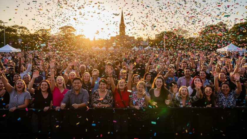 A wide-angle, vibrant photograph capturing an epic, joyous moment at a community festival in Warragul, featuring a diverse crowd cheering and confetti falling under a dramatic, sunset-lit sky, showcasing Warragul professional event photography for memorable moments.