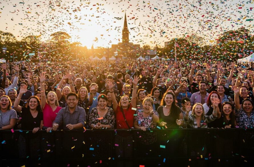 A wide-angle, vibrant photograph capturing an epic, joyous moment at a community festival in Warragul, featuring a diverse crowd cheering and confetti falling under a dramatic, sunset-lit sky, showcasing Warragul professional event photography for memorable moments.
