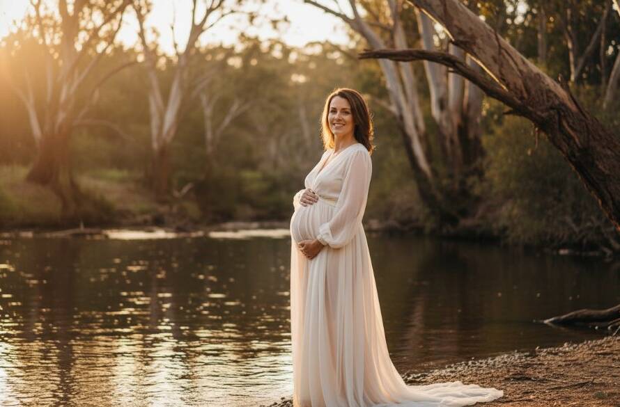 An expectant mother, in a flowing gown, stands gracefully by the tranquil Yarra River in Warrandyte, bathed in the golden light of sunset, showcasing the serene beauty of Warrandyte riverside maternity photography.