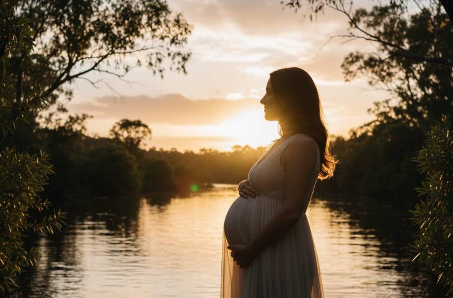 A breathtaking "Warrandyte South maternity photography natural glow" portrait of an expectant mother silhouetted against a golden hour sky, standing beside the Yarra River's serene banks at dusk, her hands cradling her belly, bathed in soft, ethereal light, professional and cinematic.