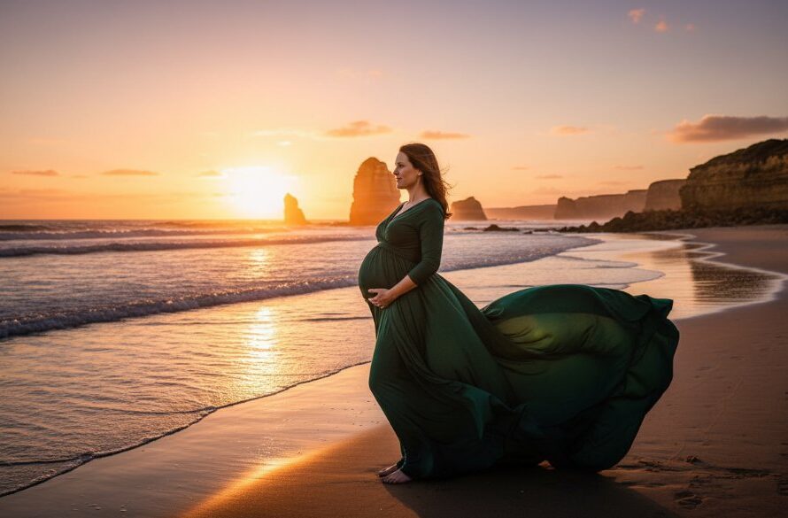 A wide, epic shot of a pregnant woman in a flowing, deep teal dress, silhouetted against a dramatic sunset over the Southern Ocean at Warrnambool, radiating an ethereal glow during her Warrnambool beach maternity photoshoot ethereal glowing session. Waves gently break on the shore, casting a serene and powerful mood.