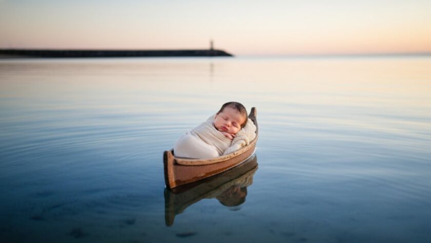A heartwarming Warrnambool newborn photography cherished moments capture: a sleeping baby swaddled in soft organic fabric, cradled gently on a rustic, weathered wooden boat, with the misty backdrop of Warrnambool's iconic coastline at dawn, bathed in soft, golden light, evoking peace and new beginnings.