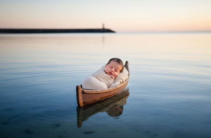 A heartwarming Warrnambool newborn photography cherished moments capture: a sleeping baby swaddled in soft organic fabric, cradled gently on a rustic, weathered wooden boat, with the misty backdrop of Warrnambool's iconic coastline at dawn, bathed in soft, golden light, evoking peace and new beginnings.