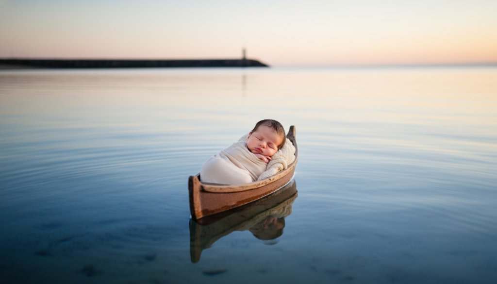 A heartwarming Warrnambool newborn photography cherished moments capture: a sleeping baby swaddled in soft organic fabric, cradled gently on a rustic, weathered wooden boat, with the misty backdrop of Warrnambool's iconic coastline at dawn, bathed in soft, golden light, evoking peace and new beginnings.