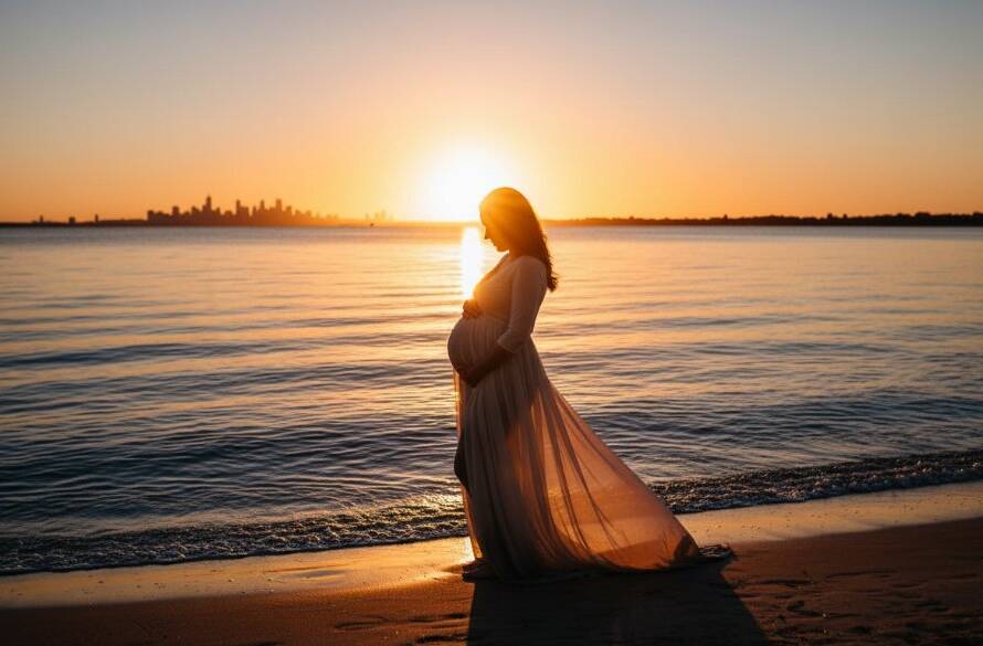 A radiant expectant mother, silhouetted against a dramatic Williamstown bay sunset, holding her belly gently, with golden light reflecting on the water. This epic Williamstown maternity photography bay sunset moment is captured with professional grading and stunning detail.