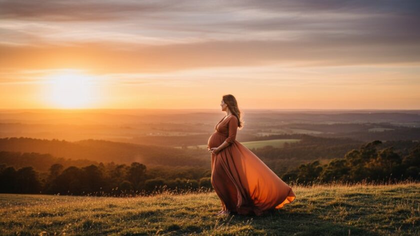 An ethereal Woodend maternity photography stunning landscape portraits scene featuring a pregnant woman in a flowing gown at sunset, silhouetted against a dramatic, rolling hill landscape, bathed in golden light.