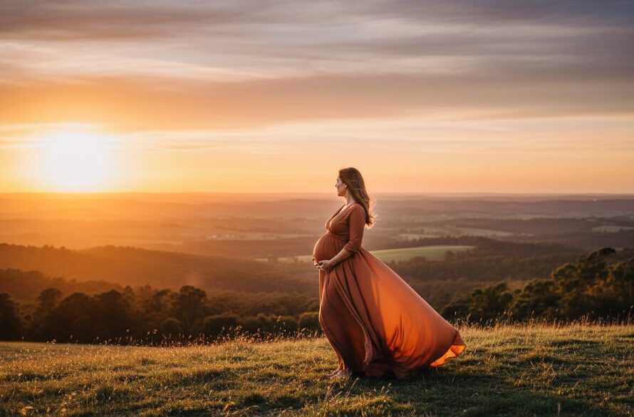 An ethereal Woodend maternity photography stunning landscape portraits scene featuring a pregnant woman in a flowing gown at sunset, silhouetted against a dramatic, rolling hill landscape, bathed in golden light.